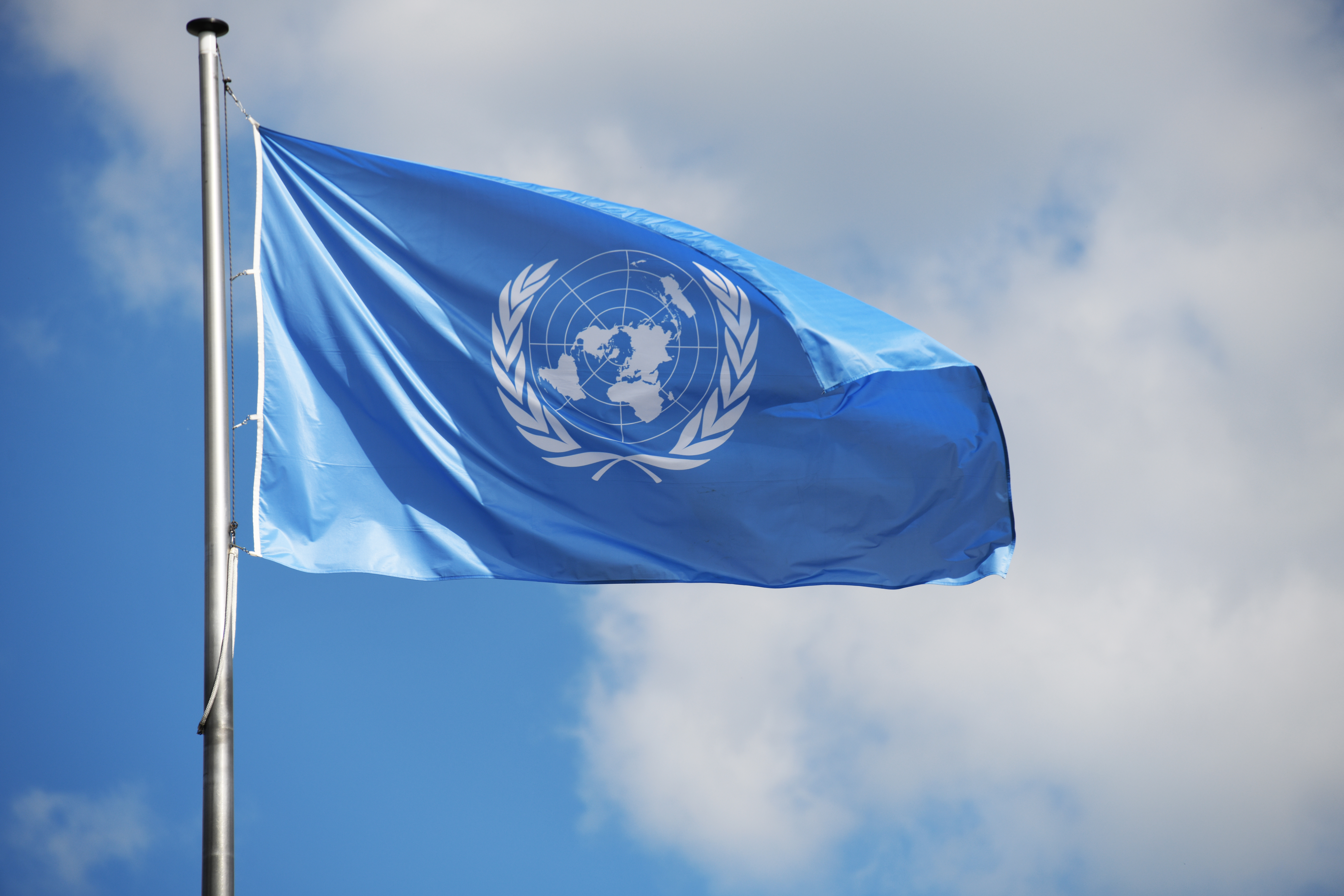 Blue UN Flag flaps against a backdrop of blue sky and clouds.